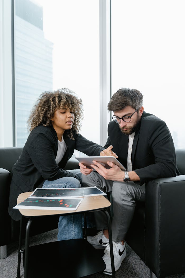 Two colleagues analyzing financial data and charts indoors using a digital tablet.