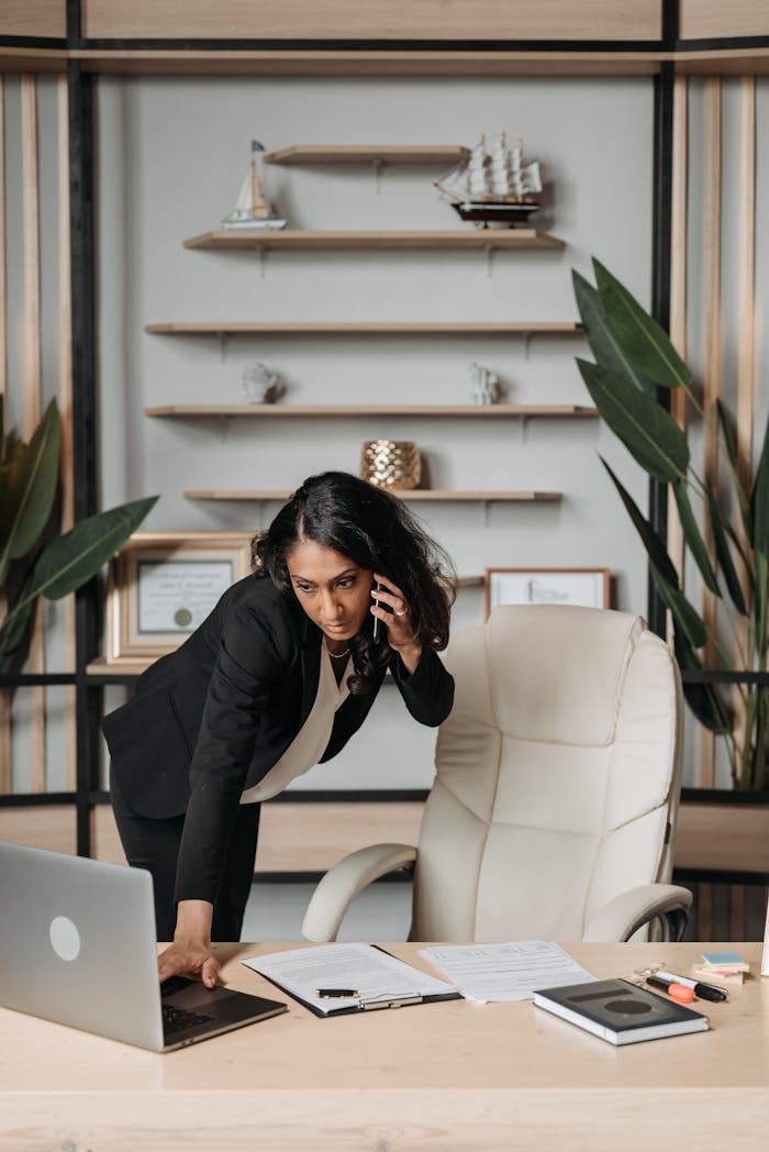 Professional woman in office multitasking with laptop and phone call.